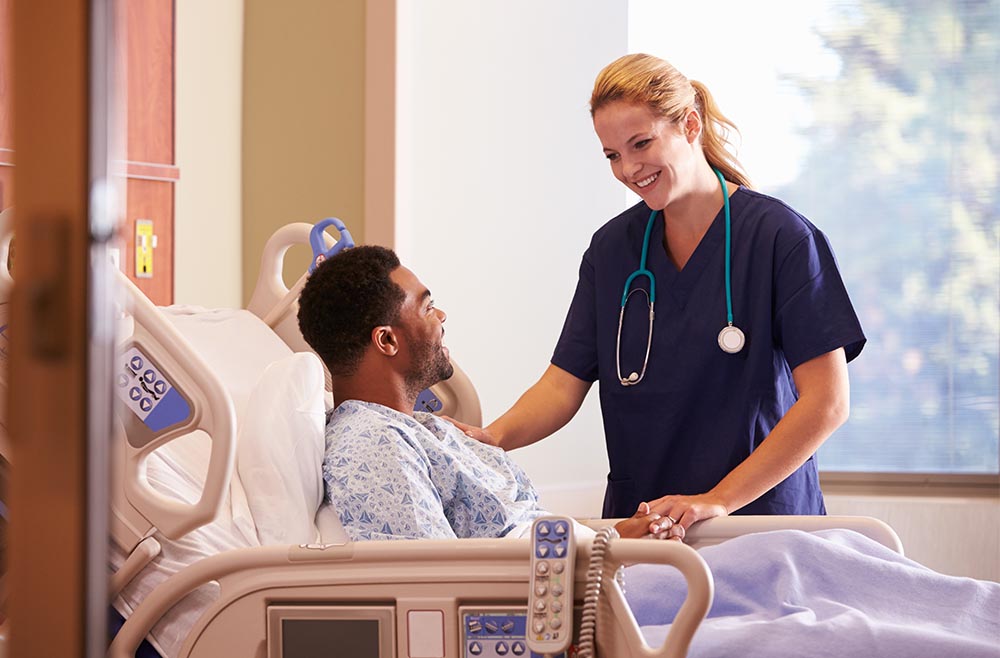 Female clinician smiling at patient in hospital bed